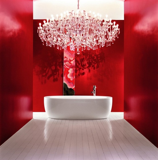 a refined bathroom with red walls, a large crystal chandelier, an oval tub and nothing else looks dreamy