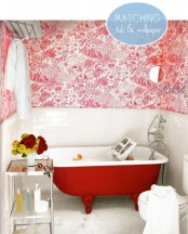 a red and white vintage bathroom with printed wallpaper, white tiles, a red tub, chic furniture and bright blooms