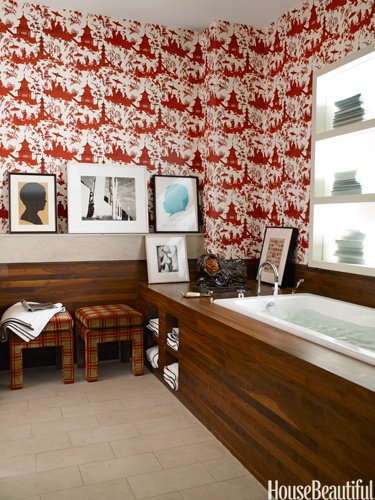 a creative bathroom with red and white wallpaper, wood clad bathtub and printed stools looks unusual