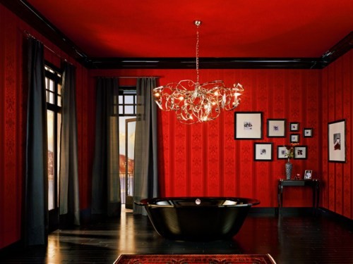 a Gothic bathroom in red and black, with a black tub and curtains, a crystal chandelier and a gallery wall