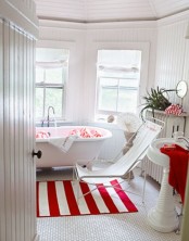 a traditional white bathroom with white furniture, a tub, potted plants and touches of red here and there