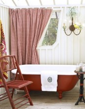 a red and white traditional bathroom with a printed curtain, a red bathtub and red furniture and a vintage chandelier