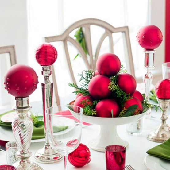 a bold and contrasting Christmas tablescape with white porcelain, red ornaments on stands and in a bowl, greenery and green napkins
