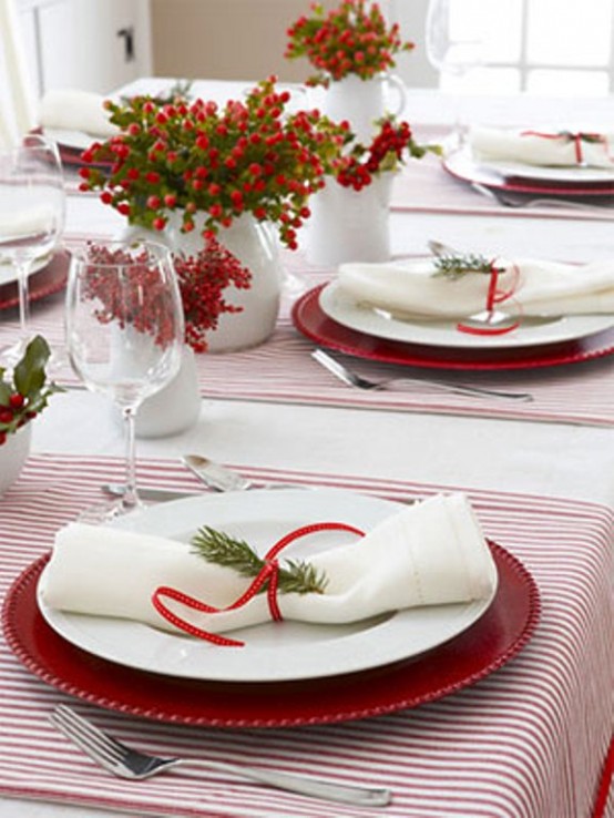 a bold red and white Christmas tablescape with striped placemats, red chargers and white porcelain, napkins with red ribbons and red berries in vases as centerpieces