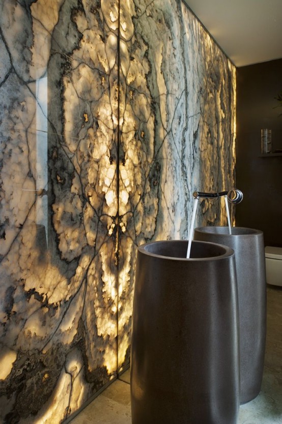 a luxurious moody bathroom with an onyx accent wall that is lit up and black free-standing sinks is an adorable space