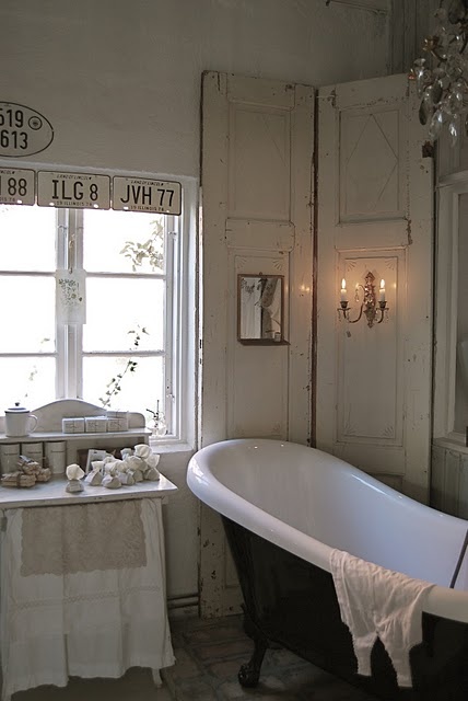 a neutral shabby chic bathroom with a black clawfoot bathtub, white shabby space dividers, a lovely vanity and vintage signs is delicate and subtle