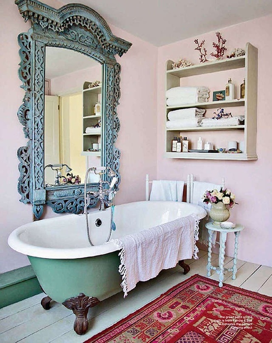 a vintage pink bathroom with a green clawfoot bathtub, with a shelving unit on the wall, a large mirror in an ornated frame, a bright rug and shabby chic furniture