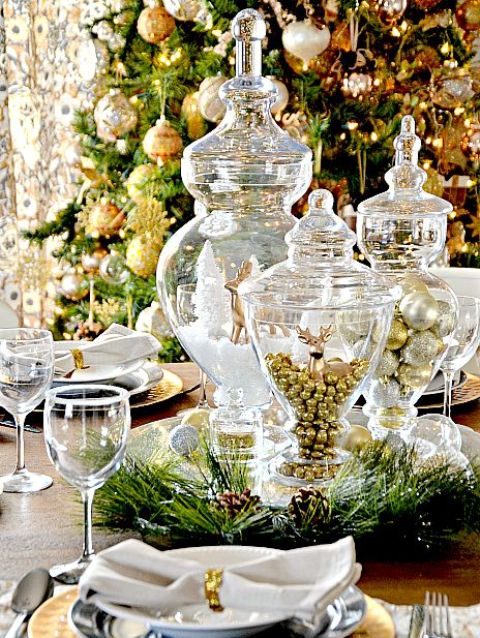 an exquisite gold and white Christmas tablescape with jars with faux snow, white and gold ornaments and a deer figurine, white napkins with gold rings and gold chargers