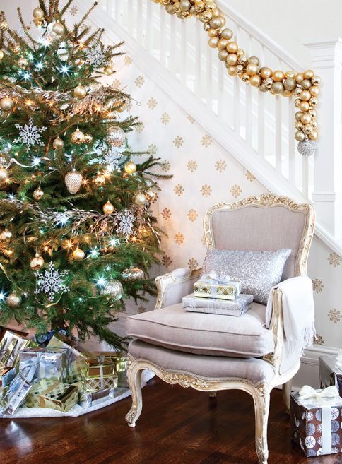 a gold ornament garland on the railing, a Christmas tree with silver and gold ornaments, lights and white snowflakes