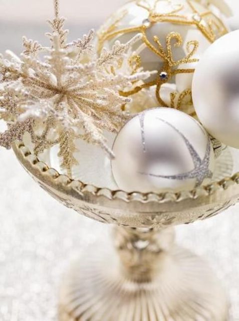 a tall glass stand with delicate and refined white and gold Christmas ornaments and an oversized glitter snowflake is amazing as a centerpiece