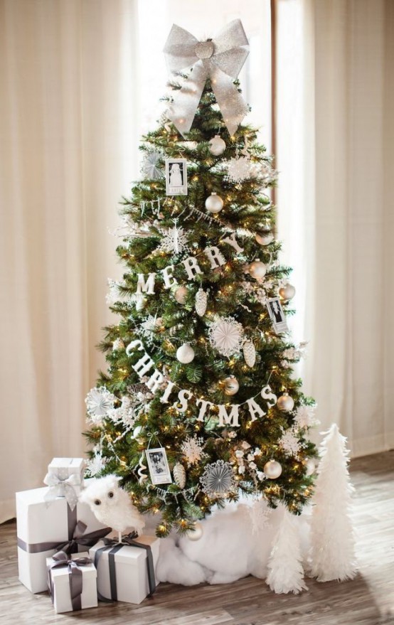 a sophisticated Christmas tree with lights, with white and gold ornaments, photos, buntings and paper pompoms plus a silver bow on top