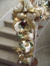 refined gold and white Christmas railing decor with gold and white embroidered ribbons and a bow, ornaments, pinecones and lights