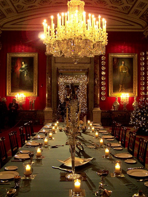 a sophisticated Gothic dining space with red walls, a jaw dropping chandelier, a long table with candles and refined artworks