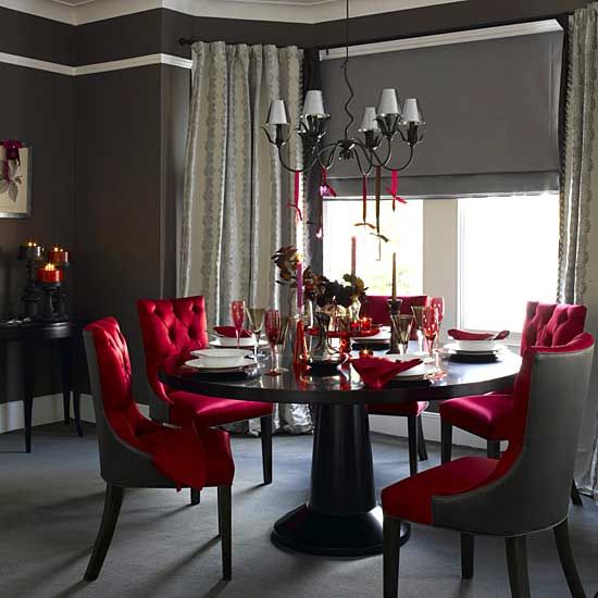 a sophisticated Gothic dining space wiht a black round table, red upholstered chairs, a vintage chandelier and red candles and glasses