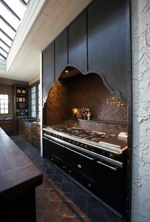 a dramatic Gothic kitchen in dark shades, with an oversized black cooker with a stone backsplash and a built-in catchy hood over the cooker