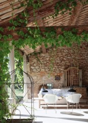 a Provence outdoor-indoor space with lots of vines, a white sofa, a coffee table and some chairs, a sideboard and vintage cages for decor