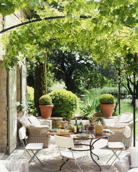 an elegant Provence terrace with a greenery roof, a round table and metal chairs, wicker chairs and potted greenery is awesome and veyr elegant
