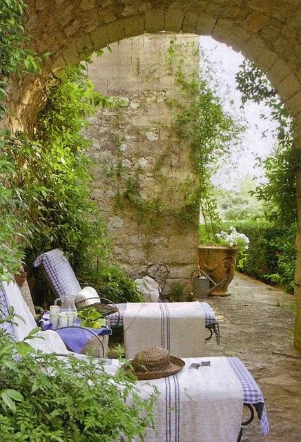 a delicate Provence terrace with loungers covered with white and blue covers, with greenery and blooms, some vintage urns
