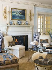 an exqusite creamy and gold living room with gorgeous molding on the walls and ceiling, a fireplace, some chic furniture, touches of blue and cool artworks