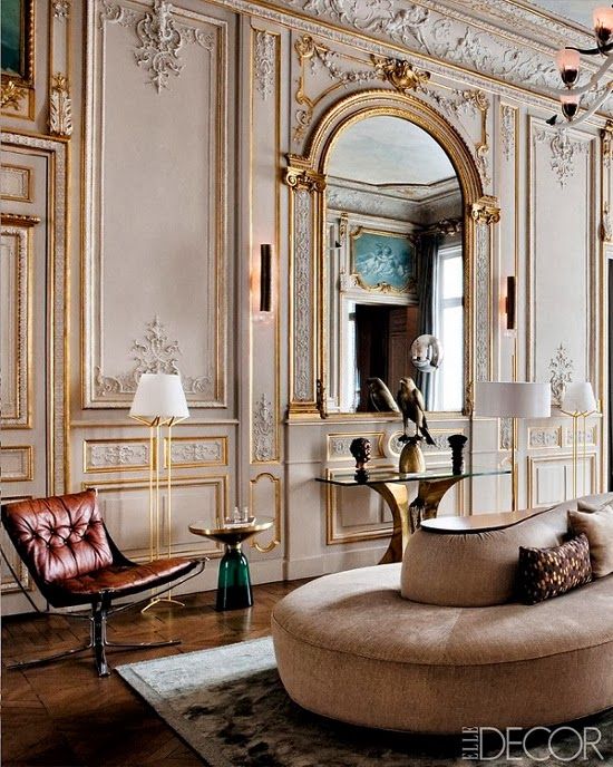 a jaw dropping space with tan walls and gold molding, with an oversized mirror, with fab furniture that matches in color and style
