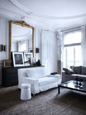 a sophisticated Parisian-inspired living room with white walls and a ceiling detailed with refined molding, with simple white furniture and a mini gallery wall plus an oversized mirror