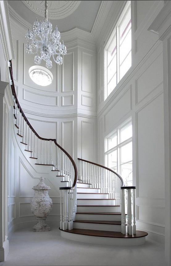 a super refined all-white space with elegant molding on the walls, a crystal chandelier and a ceiling medallion that highlights it a lot