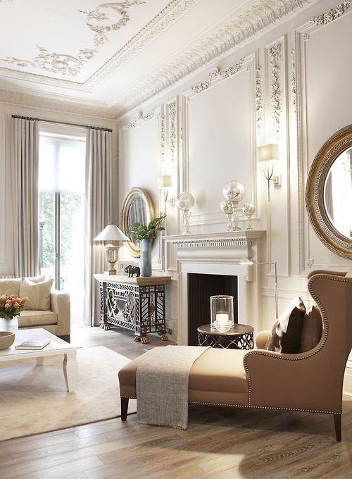 a super refined neutral interior with molding on the walls, a ceiling with molding, a fireplace, round mirrors and a tan leather chair