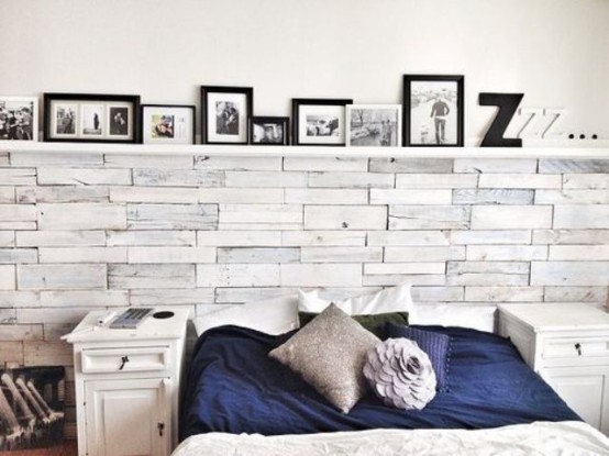 a modern rustic bedroom with a whitewashed wooden wall, white nightstands, a ledge with lots of artworks and contrasting bedding