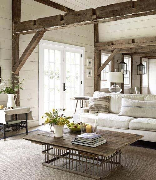 a farmhouse living room with whitewashed wooden walls, wooden beams over the space, a wooden table, plants and blooms and table lamps