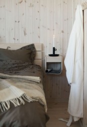 a Nordic bedroom with whitewashed walls, a wooden bed, a floating nightstand with a candle