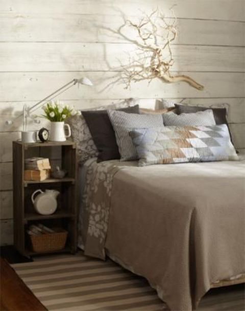 a whitewashed wooden wall, rustic furniture, printed bedding and a rug plus cool natural decor