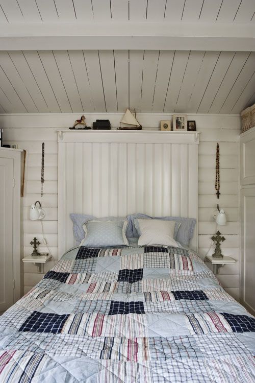 a shabby rustic bedroom with whitewashed walls and a ceiling, neutral furniture, printed bedding and sconces plus artworks