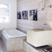 a contemporary bathroom with whitewashed walls and a floor, a bathtub clad with concrete and a black and white gallery wall to make the space bolder