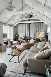 a coastal cabin living room with whitewashed wooden walls and a painted ceiling, comfortable furniture, a hearth and some vintage pendant lamps