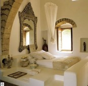 a creamy Moroccan bedroom with a zen feel, with a bed on the floor, some seats, lovely accessories and a vintage framed mirror and a canopy over the bed