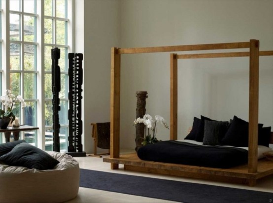 an Asian bedroom with a strong zen feel, with a wooden bed and black bedding, a neutral chair and black carved pillars as decor