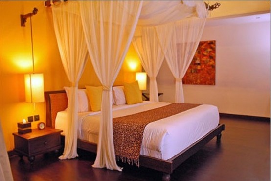 a zen bedroom with low dark wooden furniture, a canopy over the bed, some table lamps and a bright artwork