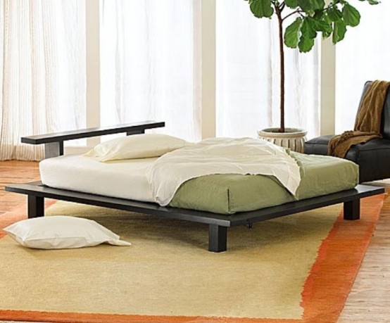 a neutral zen bedroom with a low black bed, a black leather chair, green and white bedding and a statement plant