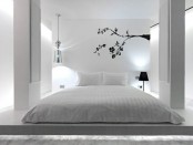 a pure white bedroom with a bed on the floor, pillars, a pendant and a floor lamp and a black blooming branch decal on the wall