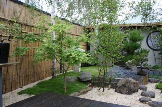 white pebbles, rocks, grass and thin trees plus a bamboo wall for a Japanese garden or front yard