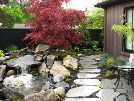 grandes tejas de roca, vegetación, musgo, rocas y una cascada y un arce rojo para darle un toque japonés