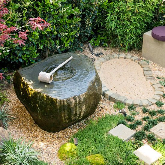 Hierba, guijarros, ladrillos y una fuente de piedra con una pala de madera para crear un ambiente japonés informal y relajado en el jardín.