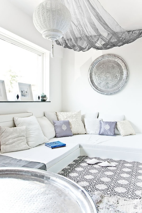 a pure white Moroccan living room with a mosaic floor, an L-shaped sofa, a traditional lantern and a hammered plate on the wall