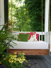 a stained wooden hanging bed with a white cushion and colorful pillows is a peaceful idea for a porch
