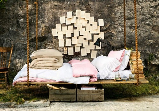 a rustic wooden hanging bed with books and pillows, some crates under it and some vintage book pages on the wall