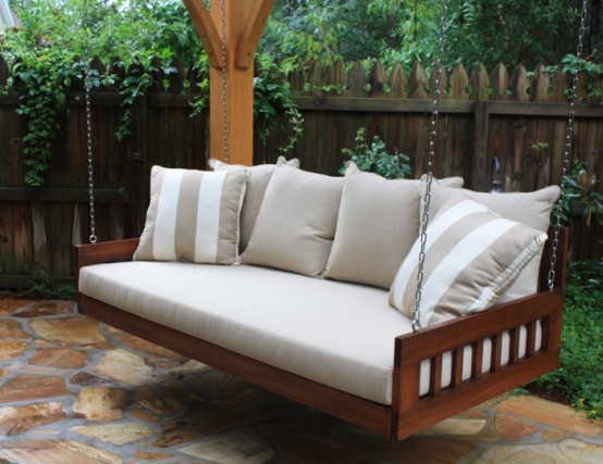 a hanging wooden bench on chains with a cushion and lots of pillows is a cool relaxing piece for any outdoor space