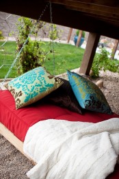 a simple hanging bed on chains with colorful bedding, blankets and pillows is a cool idea for every outdoor space