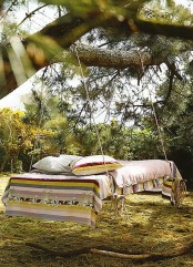a comfy hanging bed on ropes hanging on a tree with colorful boho bedding feels and looks very inviting