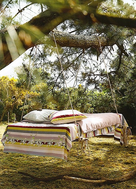 a comfy hanging bed on ropes hanging on a tree with colorful boho bedding feels and looks very inviting