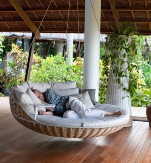a wicker outdoor hanging bed with a side table and lots of pillows plus ropes is a gorgeous idea for any outdoor space